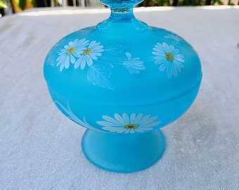 May include: A light blue glass candy dish with a white floral design. The dish has a round base and a lid with a knob on top.