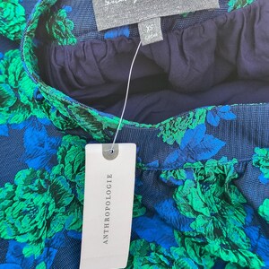 May include: Close-up of a skirt with a floral pattern in shades of blue and green. The skirt has a navy blue waistband and lining. A tag from Anthropologie is attached. The label reads "Sunday in Brooklyn".
