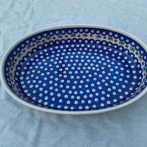 May include: Oval ceramic serving dish with a white rim and a blue interior. The interior is decorated with white dots and a border of floral and geometric patterns in blue, green, and brown.
