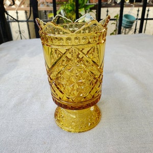 May include: A yellow glass vase with a diamond pattern and a scalloped rim. The vase has a wide base and a narrow neck.