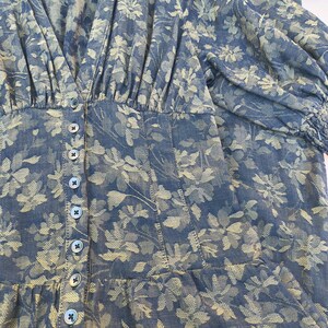 May include: A blue floral print dress with a V-neckline and button-down front. The dress features a fitted bodice, long sleeves, and a ruffled hem. The floral pattern is in shades of beige and blue.