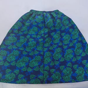 May include: A full-length skirt with a vibrant floral pattern. The skirt features a deep blue background adorned with large green and teal rose blooms. The fabric is gathered at the waist, creating a flowing silhouette.
