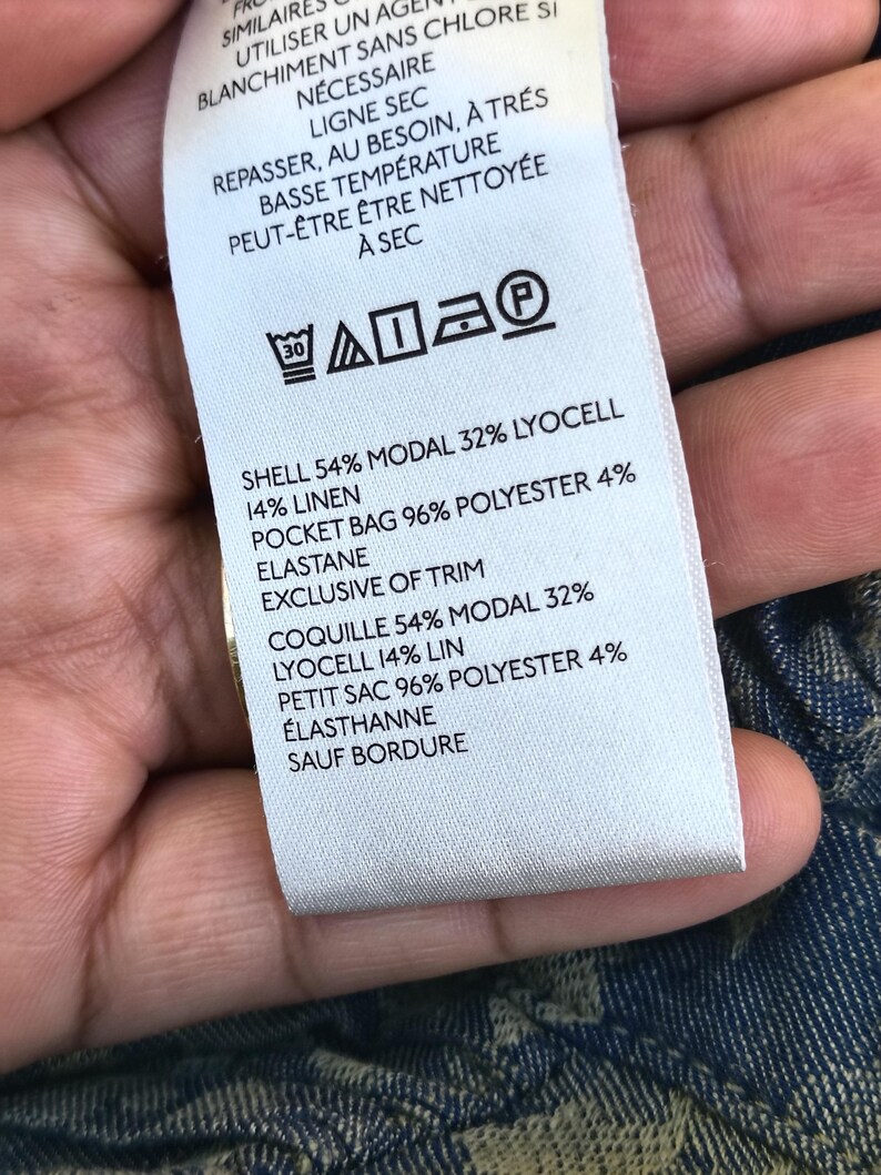 May include: A white clothing tag with black text detailing fabric composition and care instructions. The tag lists the shell as 54% modal, 32% lyocell, and 14% linen. It also includes washing symbols and the text "EXCLUSIVE OF TRIM."