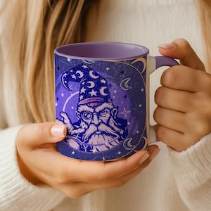 May include: A white ceramic mug with a purple interior and handle. The mug features a wizard illustration in shades of blue and purple, with stars and crescent moons. The wizard wears a pointed hat and has a long white beard.