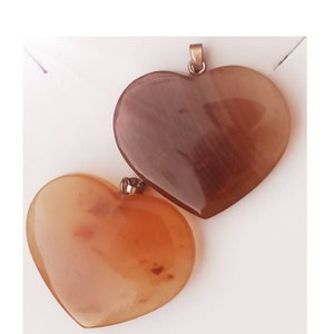 May include: Two heart-shaped carnelian pendants, one is a darker brown color and the other is a lighter orange color. Both pendants have a shiny, polished finish.