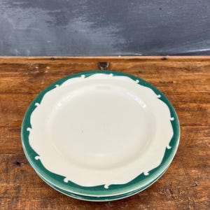 May include: Two white ceramic plates with a green scalloped border. The plates are stacked on top of each other.