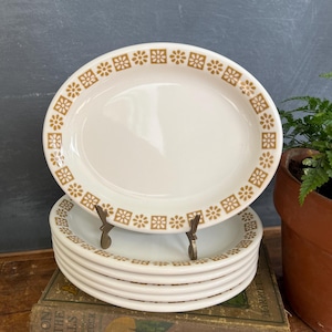 May include: A stack of six white ceramic salad plates with a brown floral pattern around the rim.