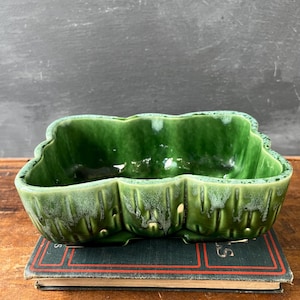 May include: A rectangular ceramic planter with a scalloped edge and a deep green glaze. The exterior features a vertical ribbed texture with lighter green drip-style accents along the top rim and base, creating a glossy finish on the vessel.