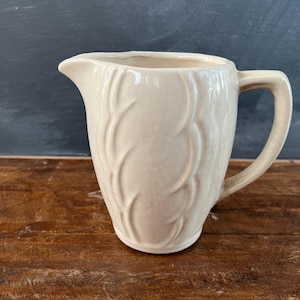 May include: A white ceramic pitcher with a textured, leaf-like design. The pitcher has a rounded body and a handle.