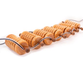 May include: A set of wooden massage rollers in a light brown hue. The cylindrical rollers feature carved grooves and are strung on a silver wire. Each roller has a small, round wooden knob at each end, designed for massage.