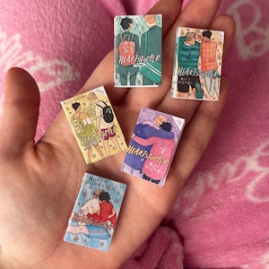 Può includere: Una collezione di cinque graphic novel, tutte con il titolo "Heartstopper" sulla copertina. Le copertine presentano illustrazioni di due giovani uomini, con scene e colori diversi su ogni copertina. I libri sono tutti nello stesso stile, con uno sfondo bianco e testo nero.