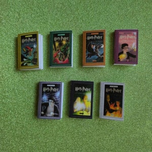 Puede incluir: Un conjunto de siete libros en miniatura de tapa dura de la serie Harry Potter. Los libros están dispuestos en dos filas, con la primera fila mostrando los libros 1-3 y la segunda fila mostrando los libros 4-6. Las cubiertas de los libros presentan ilustraciones de la serie, incluyendo Harry Potter, Ron Weasley, Hermione Granger y otros personajes.