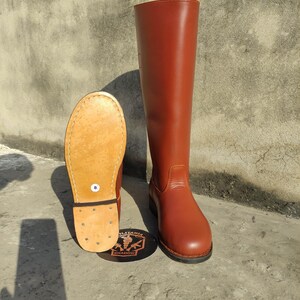 May include: A pair of brown leather riding boots. One boot is upright, the other is lying on its side, revealing the sole. The boots are a reddish-brown color and have a classic design. The sole of the boot is a light tan color. The boots are size 8.