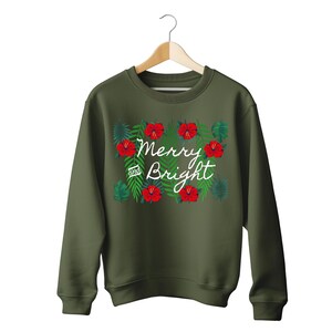 May include: An olive green sweatshirt with the words "Merry and Bright" in white script, surrounded by red hibiscus flowers and green leaves. The sweatshirt is hanging on a wooden hanger.