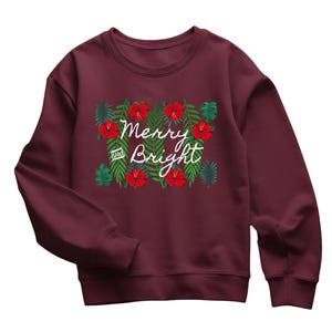 May include: Burgundy sweatshirt with a floral design featuring red hibiscus flowers and green leaves. The words "Merry and Bright" are written in white script across the front. A festive holiday-themed top.