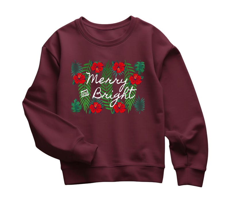 May include: Burgundy sweatshirt with a floral design featuring red hibiscus flowers and green leaves. The words "Merry and Bright" are written in white script across the front. A festive holiday-themed top.