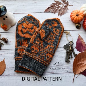 May include: A pair of knitted gray and orange mittens with a pumpkin design. The mittens are surrounded by pumpkins, leaves, and keys on a white wooden surface. The text "DIGITAL PATTERN" is visible.
