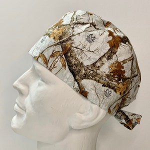 May include: A white, brown, and tan camouflage patterned surgical scrub hat with the Realtree Edge logo.