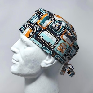 May include: A patterned scrub cap featuring a repeating design of retro-style vans in shades of teal, orange, and white on a navy blue background. The cap is tied at the back and displayed on a white mannequin head.