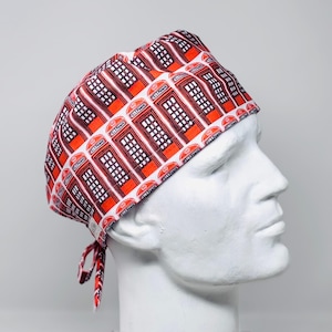 May include: A scrub cap featuring a repeating pattern of red British telephone boxes on a white background. The fabric cap has a rounded crown and ties at the back, displaying the word TELEPHONE printed on each individual booth graphic.