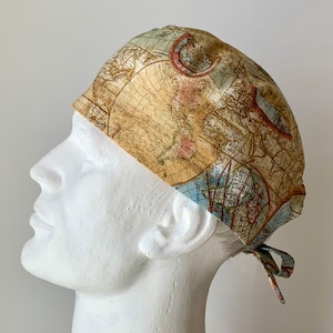 May include: A surgical scrub hat with a vintage world map print in shades of brown, blue, and beige. The hat has a tie at the back.