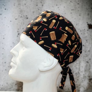 May include: Black scrub hat with a repeating pattern of brown logs and red axes. The hat has a tie at the back.
