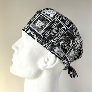 May include: Black and white patterned scrub hat with a Christmas theme. The hat features images of a Christmas tree, a cup of hot cocoa, a reindeer, and the words "Christmas Tree Farm".