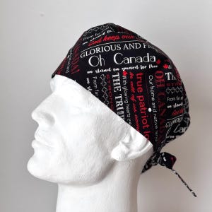 May include: Black scrub hat with red and white text that reads "God keep our glorious and free Oh Canada we stand on guard for thee with glowing hearts we true patriot love our home and native land".