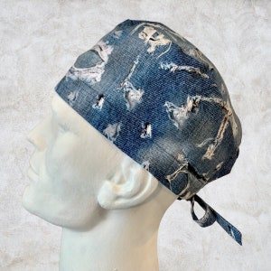 May include: A blue denim scrub hat with a distressed look and white stitching. The hat has a tie at the back.