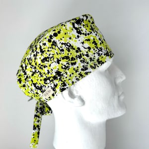 May include: A green, black, and white patterned surgical scrub hat with a tie. The hat has a splatter paint design.