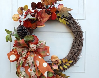 May include: A fall-themed wreath with a brown twig base, decorated with faux leaves, berries, and a bow with white polka dots. The wreath features a variety of fall colors, including orange, red, and brown.