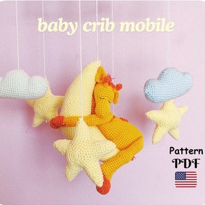Puede incluir: Un móvil de cuna de crochet con una luna creciente amarilla, una estrella amarilla, una nube azul y una jirafa amarilla durmiendo en la luna. El texto "baby crib mobile" y "Pattern PDF" es visible en la imagen. La bandera estadounidense también es visible en la imagen.
