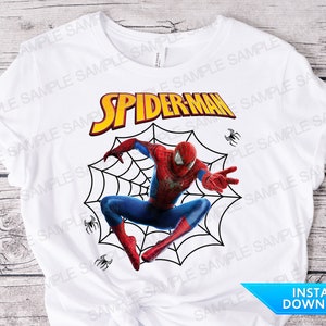 Könnte beinhalten: Weißes T-Shirt mit einer roten und blauen Spiderman-Grafik auf einem schwarzen Netz. Der Text "SPIDER-MAN" ist in gelben Buchstaben.