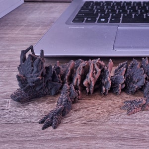 Könnte beinhalten: Ein detailliertes, artikuliertes, braunes und schwarzes Plastikmodell eines Drachen mit einem stacheligen Rücken und Schwanz. Der Drache ist auf einer Holzoberfläche platziert.