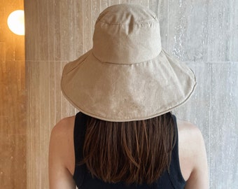 Pode incluir: Um chapéu de sol bege de aba larga feito de tecido texturizado. O chapéu tem um design simples e uma coroa plana.