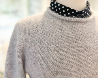 May include: A gray knitted sweater with a round neckline. The sweater is on a mannequin wearing a black and white polka dot shirt.
