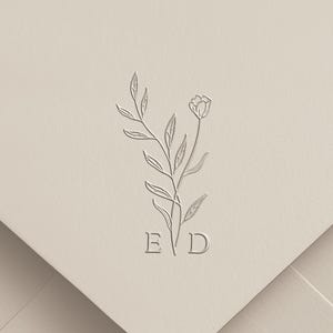 May include: A light beige envelope featuring a centered, embossed line art illustration of a single floral stem with leaves. The letters E and D are positioned at the base of the stem, integrated into the embossed design on the paper surface.
