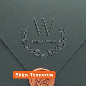May include: A dark gray envelope featuring an embossed letter W, the names DALIA & ADRIAN, and a floral wreath design. A copper-colored wax seal with a rose pattern is positioned at the bottom, and an orange label reads Ships Tomorrow.