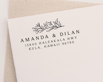 May include: A white card with a black ink stamp featuring a simple floral design and the text "Amanda & Dilan 15840 Haleakala Hwy Kula, Hawaii 96790".