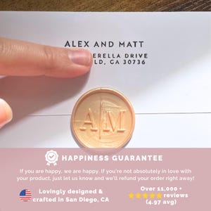May include: A gold wax seal with the initials "AM" pressed into it. The seal is on a white envelope with the text "ALEX AND MATT ERELLA DRIVE LD, GA 30736" printed on it. The text "HAPPINESS GUARANTEE" is printed below the seal. The text "If you are happy, we are happy. If you're not absolutely in love with your product, just let us know and we'll refund your order right away!" is printed below the text "HAPPINESS GUARANTEE". The text "Lovingly designed & crafted in San Diego, CA" is printed below the text "HAPPINESS GUARANTEE". The text "Over 11,000 reviews (4.97 avg)" is printed below the text "Lovingly designed & crafted in San Diego, CA".