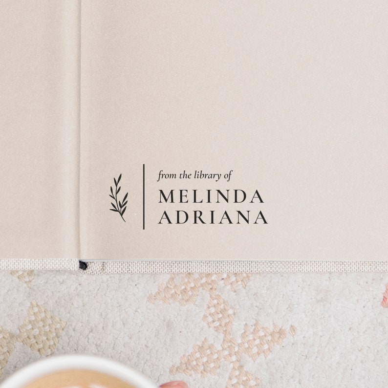 May include: A book with a cream-colored cover and a black stamp that reads "from the library of MELINDA ADRIANA" with a small branch design.