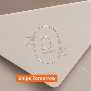 May include: Cream-colored envelope with a debossed oval design featuring the letter "D" and the name "Daniels". The design is framed by delicate leaf accents. The text "Ships Tomorrow" is in an orange rectangle.