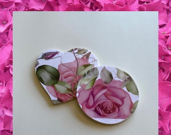 Puede incluir: Dos posavasos florales rosas, uno en forma de corazón y otro redondo, con fondo blanco. Los posavasos presentan un diseño de estilo acuarela de rosas rosas y hojas verdes.