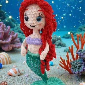 May include: A crocheted Little Mermaid doll with red hair, a purple top, and a green tail. The doll is set against a backdrop of an underwater scene with coral and seashells. The text "LITTLE MERMAID" is at the bottom.