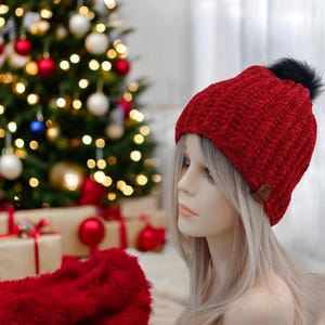 May include: A red velvet beanie with a black pom pom. The beanie is knitted and has a brown leather tag.
