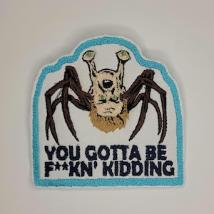 Op de afbeelding: Witte geborduurde patch met een blauwe rand. De patch toont een cartoonafbeelding van een spinachtig wezen met een menselijk gezicht en de tekst "YOU GOTTA BE F**KN' KIDDING".