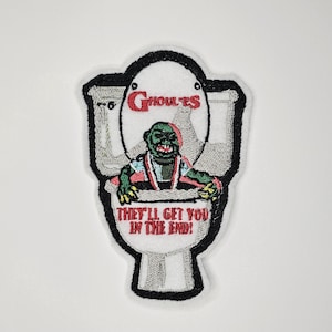 Peut inclure: Un patch brodé représentant un monstre vert assis sur des toilettes avec le texte "Ghoulies" et "They'll get you in the end!"