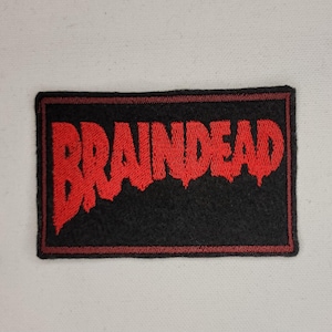 Puede incluir: Parche bordado rojo con la palabra "BRAINDREAD" en una fuente de goteo sobre un fondo negro.