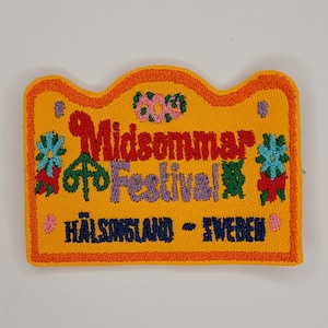 May include: A yellow embroidered patch with the text "Midsommar Festival" and "Halsingland - Sweden". The patch is decorated with colorful flowers.