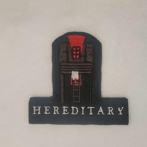 Può includere: Toppa ricamata in bianco e nero con una casa con tetto rosso e la parola "HEREDITARY" in bianco.